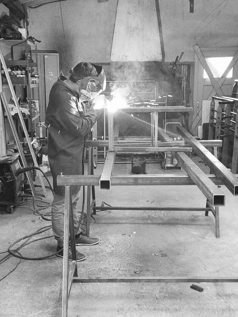 Artisan métallier de l'Atelier Steel Art en train de souder une structure en acier dans son atelier