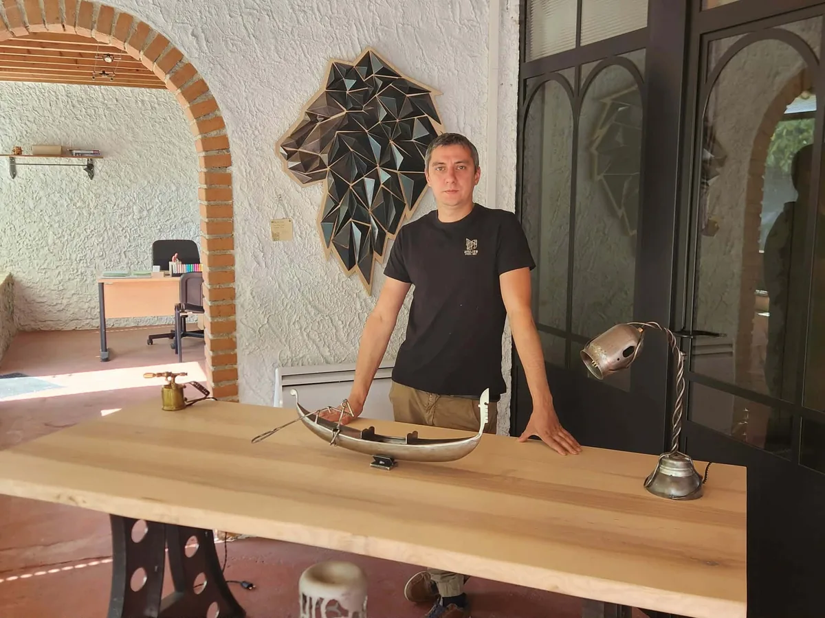Alexis Luciani, artisan métallier de l'Atelier Steel Art, dans son atelier devant une table en bois présentant ses créations en acier